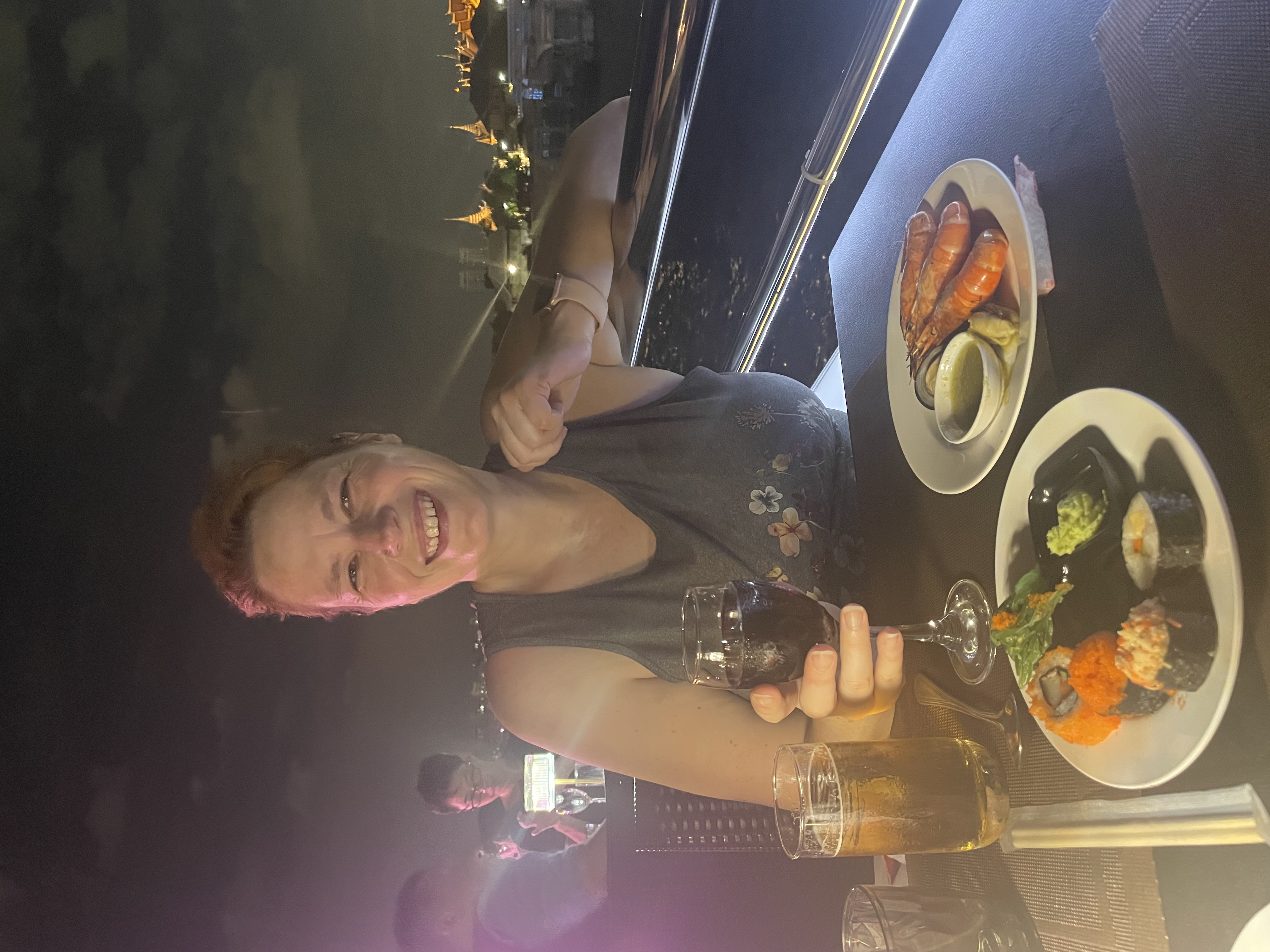 Mari at a dinner cruise on the Chao Phraya River with a temple lit up behind her